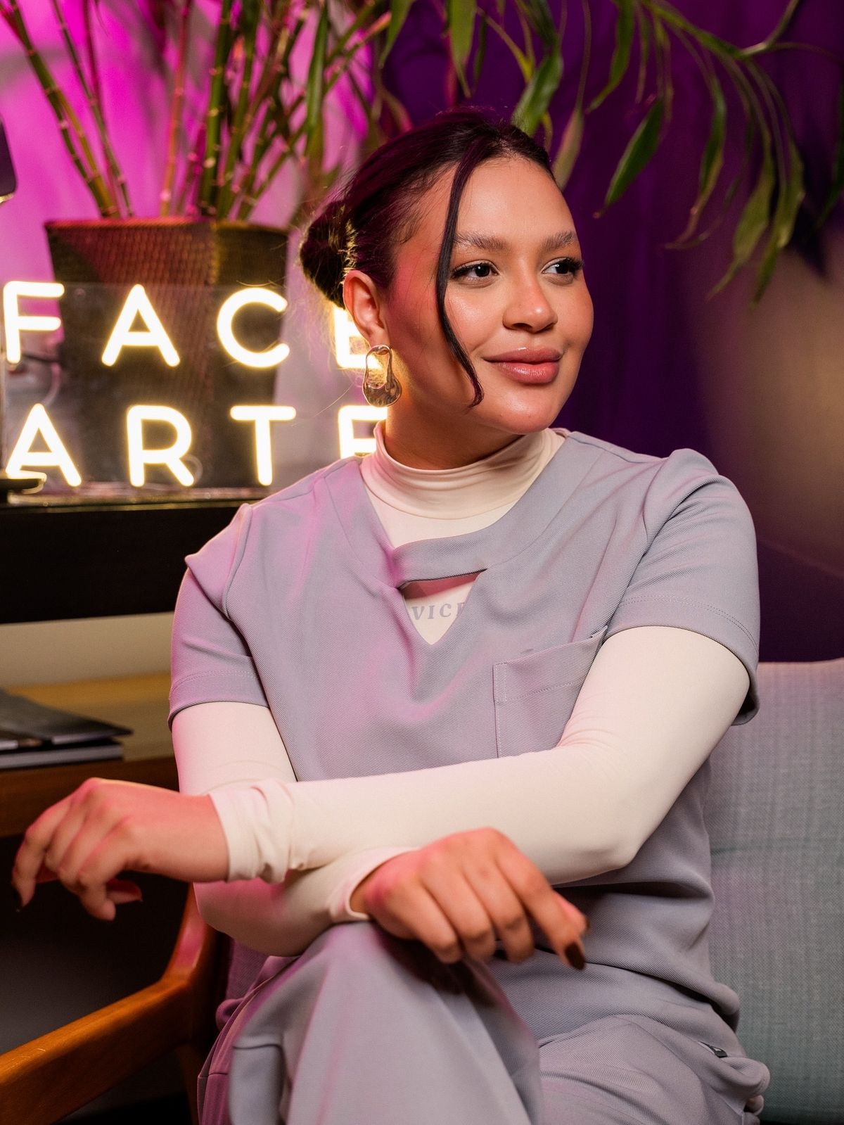 Aluna sorrindo em frente ao letreiro neon da Face Arte durante evento presencial